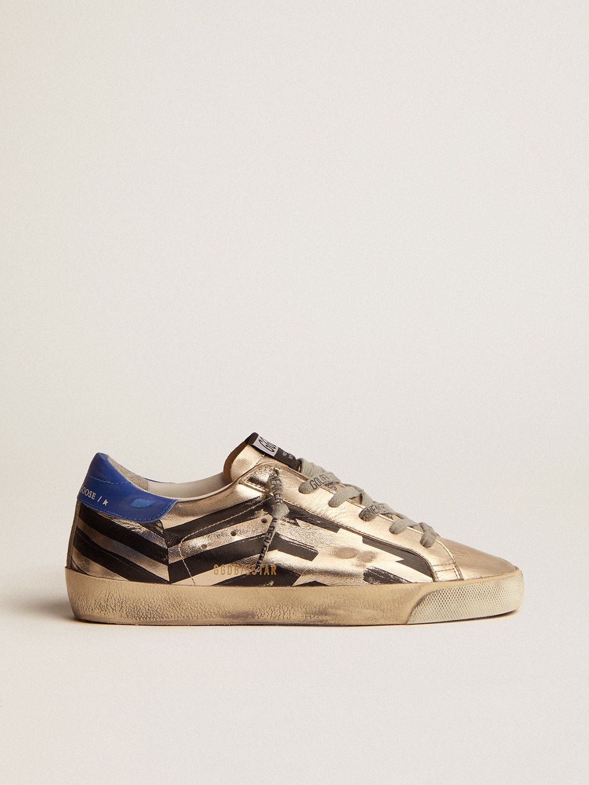 Sneakers Uomo Golden Goose Super-Star sneakers in platinum-colored laminated leather with black flag print and red and blue heel tab